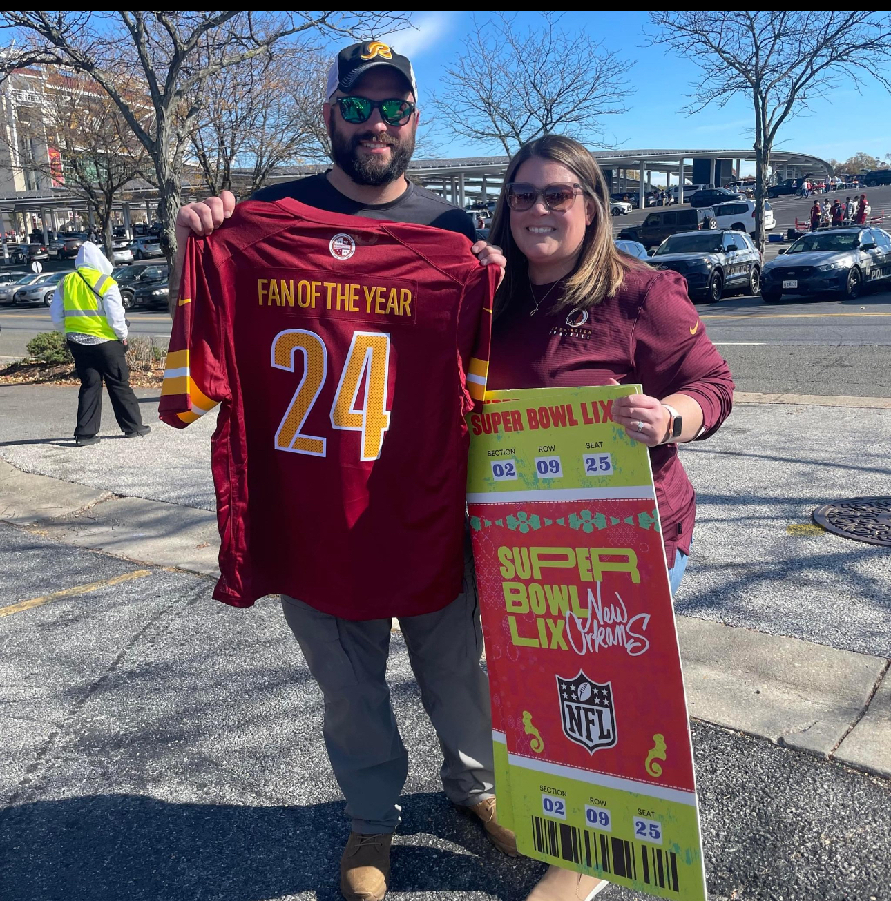 FCPS alumnus Dale McCord holds up a Washington Commanders shirt that says Fan of the Year next to a woman holding up a cardboard ceremonial Super Bowl ticket. 
 